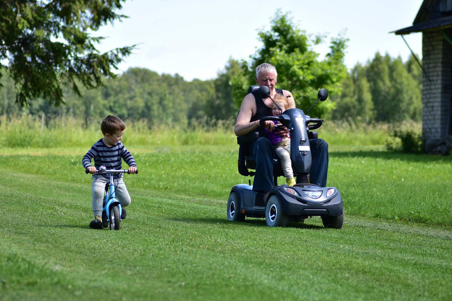 Young boy riding a balance bike beside his grandfather on a mobility scooter